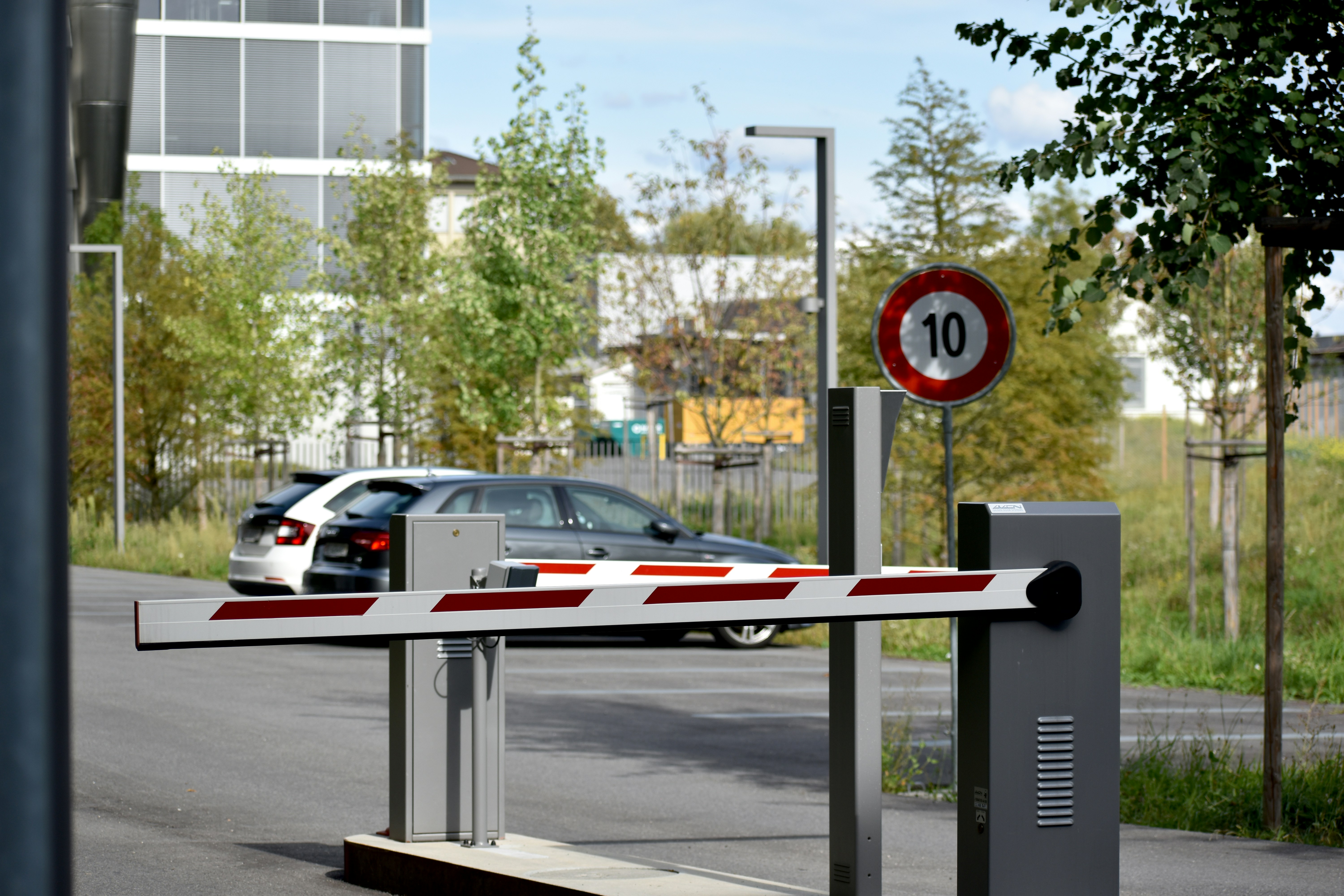 A parking gate barrier with arms down and two cars in the background